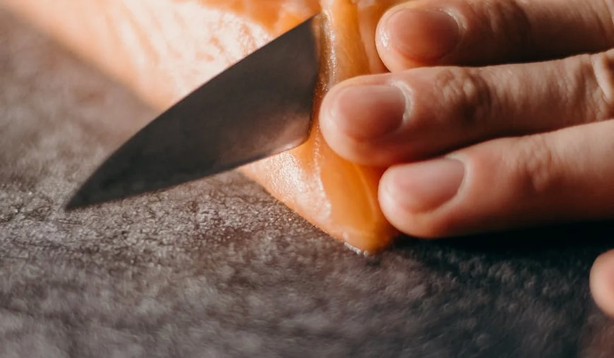 Close-up of a hand slicing a salmon fillet on a cutting board