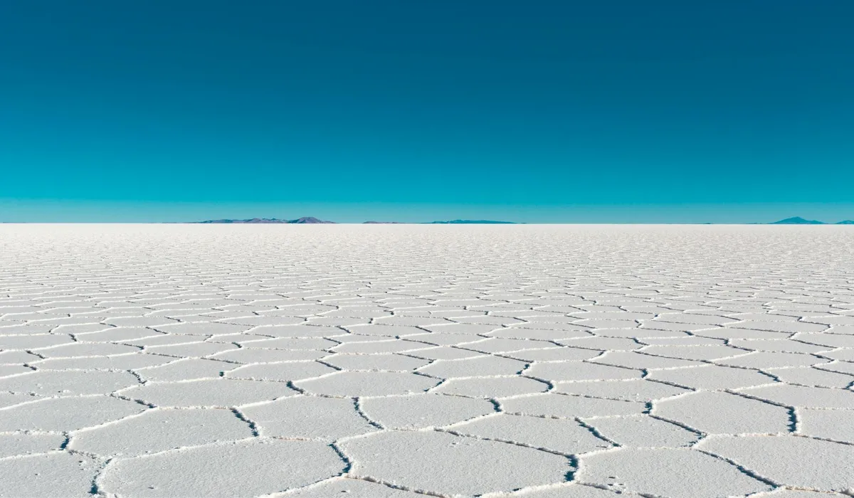 White salt flats with hexagonal crack patterns under a clear blue sky.