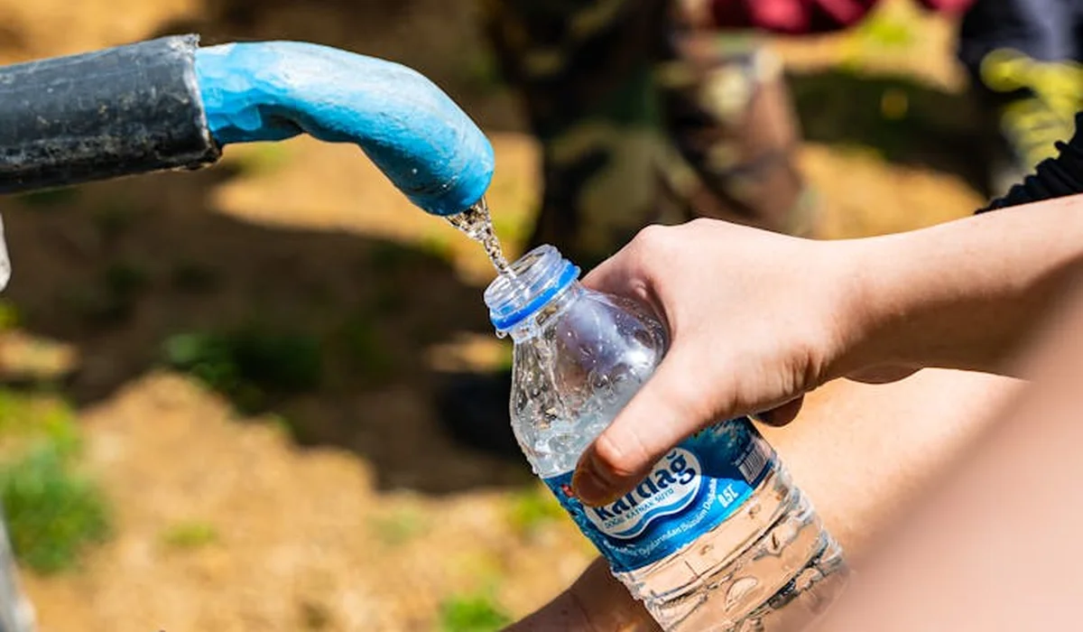 Close-up of a hand filling a plastic water bottle at an outdoor drinking fountain with water pouring into the bottle
