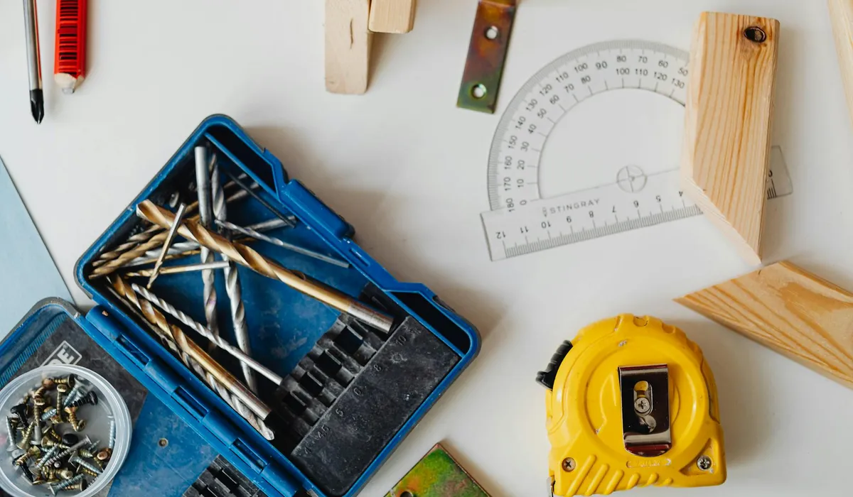 A collection of measurement tools—yellow tape measure, protractor, ruler, screws, drill bits, and wooden blocks on a white surface.