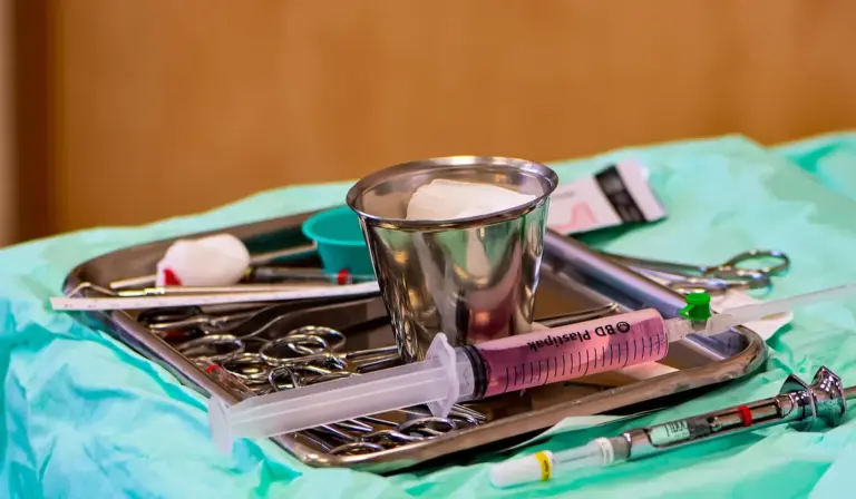Sterile medical tray with surgical instruments, including a syringe and scissors, placed on a blue drape.