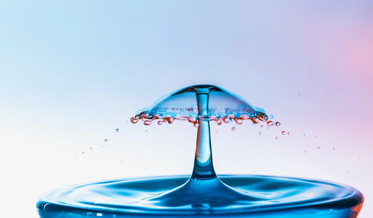 Close-up of a blue water droplet creating a splash crown on a calm water surface.